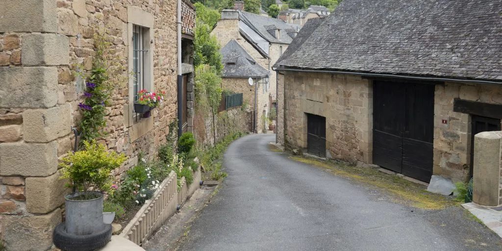 a narrow street with a stone building and a potted planter