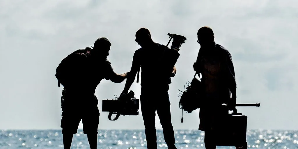 silhouette of men holding camera standing on sand near body of water during daytime